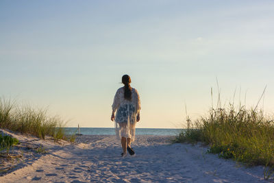 Rear view of man walking on beach against sky