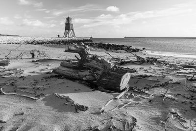 Driftwood on sand with lighthouse at beach against sky