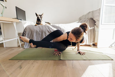 Woman practicing yoga on exercise mat in bedroom at apartment