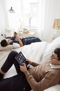 Brothers lying on bed and using phone and tablet