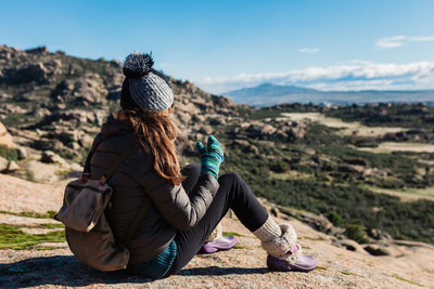 Rear view of woman sitting on rock against sky