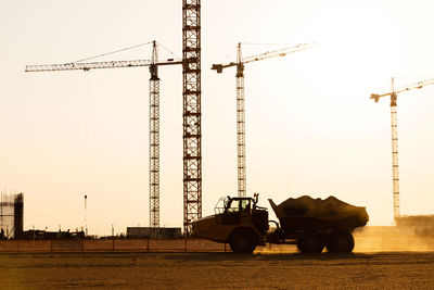 Group tower cranes silhouette of dump truck at construction site, sunset sky background. 