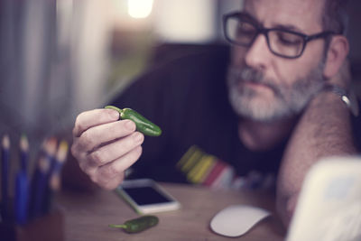 Thoughtful man holding green chili pepper at desk in workshop
