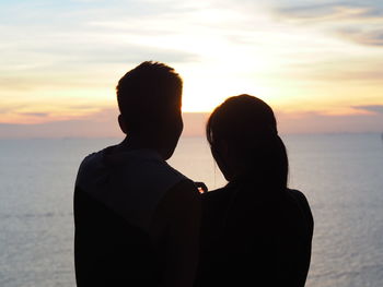 Rear view of couple standing at beach during sunset