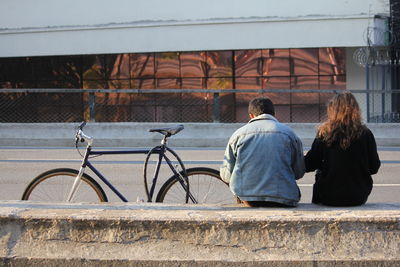 Rear view of couple sitting on retaining wall by bicycle