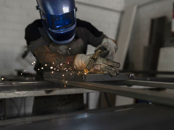 Unrecognizable male welder using welding machine on metal detail while working at workbench in factory