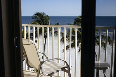 Empty chair on balcony by sea against sky