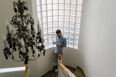 Man having coffee while using mobile phone standing on staircase at home