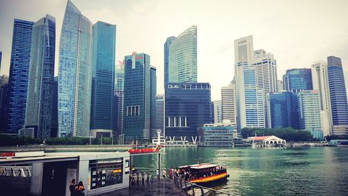 Modern cityscape by river against sky in city