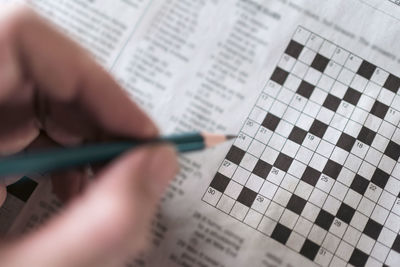 Close up hand holding pencil over crossword puzzle on newspaper. 