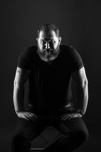 Portrait of young man sitting against black background