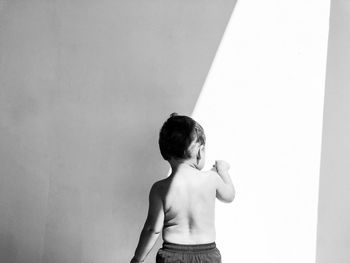 Rear view of shirtless boy standing against wall