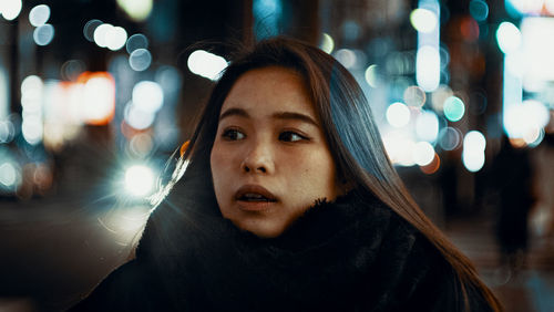 Portrait of young woman in illuminated city at night