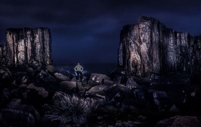 Rear view of woman sitting on rock at beach against sky at night