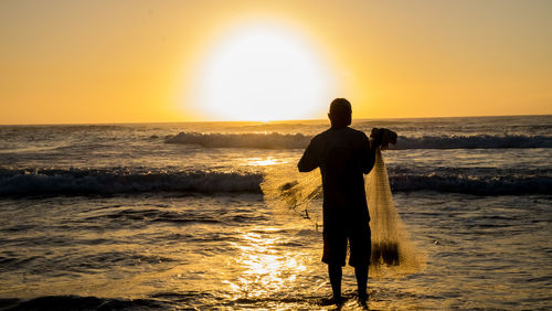 Rear view of man standing on beach against sky during sunset