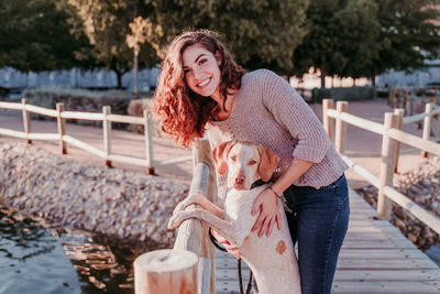 Portrait of smiling woman standing with dog on pier by lake