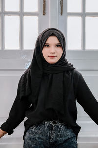 Portrait of young woman standing against wall