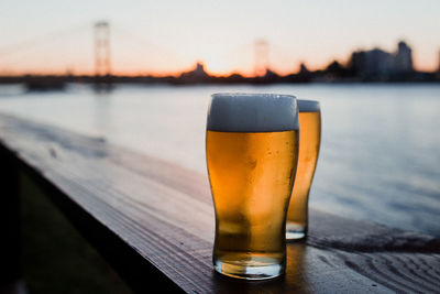 Close-up of beer in glasses on table against sky during sunset