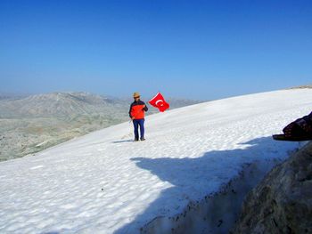 Full length of man holding turkish flag on snow covered land against sky