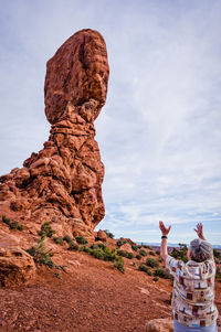 Senior woman gesturing against rock formation against sky