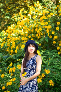 Portrait of a beautiful young woman standing by yellow flowering plants