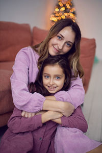 Caucasian girl with big eyes in a pink dress is sitting on a sofa with a woman mother.