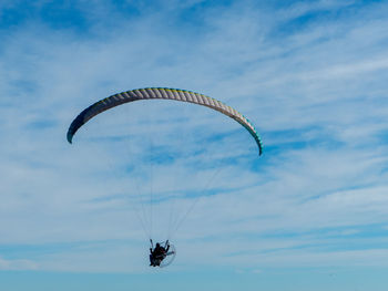 Low angle view of man paragliding against cloudy sky