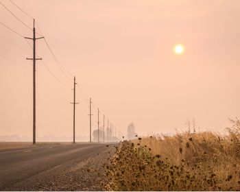 Electricity pylons on landscape against clear sky at sunset