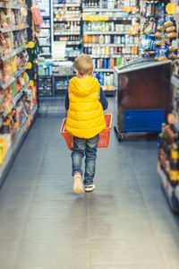 Full length rear view of boy with bucket walking in supermarket