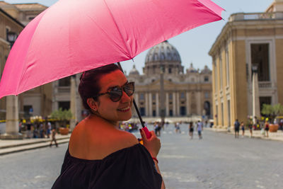 Mid adult woman holding umbrella standing in city