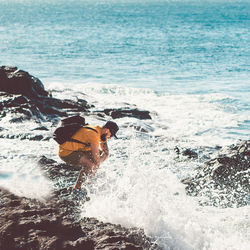 Man standing on rock by splashing water at seashore