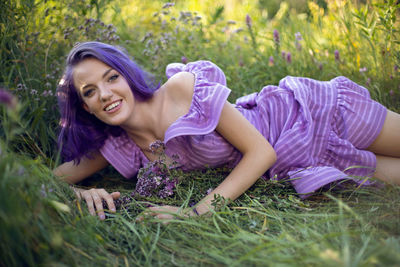 Teenage girl with dyed purple hair and a nose piercing in the grass and in a short dress