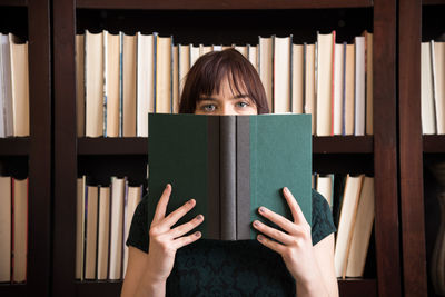 Young woman reading book against bookshelf in library