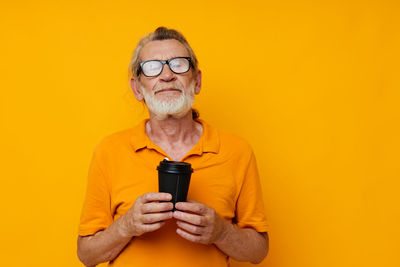 Portrait of woman holding camera against yellow background