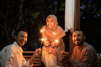 Friends holding sparkler sitting outdoors