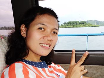 Portrait of smiling young woman gesturing while sitting in car against river