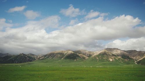 Scenic view of grassy field and mountain range against cloudy sky
