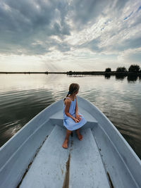Rear view of girl sitting on lake against sky