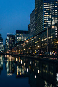 Illuminated buildings by river against sky at dusk