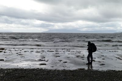 Side view of man walking on shore at beach against sky