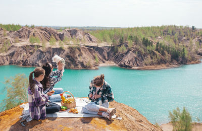 Rear view of woman sitting on rock by lake