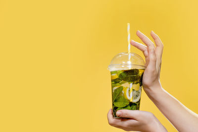 Midsection of woman holding drink against orange background