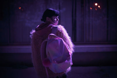 Portrait of smiling young woman standing against illuminated wall at night