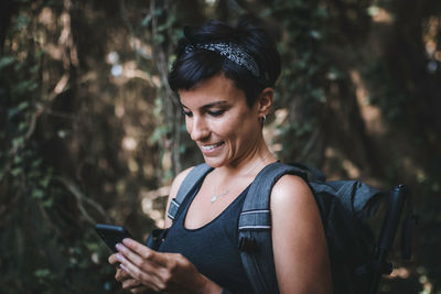 Smiling woman using smart phone while standing in forest