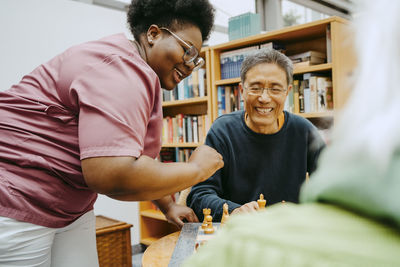 Smiling nurse playing chess with happy senior man sitting in nursing home