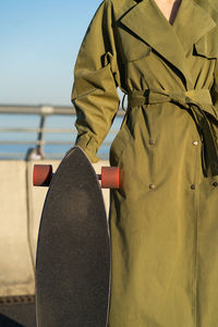 Closeup of casual girl with longboard standing over blue sky. hipster stylish woman hold skateboard