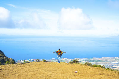 Rear view of woman standing on beach against sky