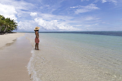 Young man with sun hat staring at turquoise sea at white sandy beach