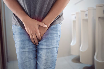 Midsection of man suffering from urinal pain in bathroom