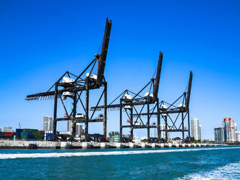 Cranes at commercial dock against clear blue sky